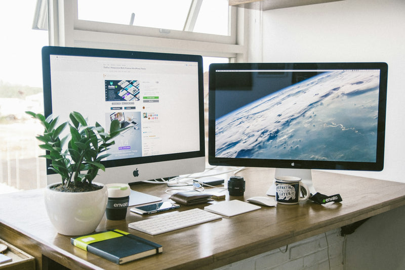 Dual monitor setup raised on arms over a clean brown wood desk