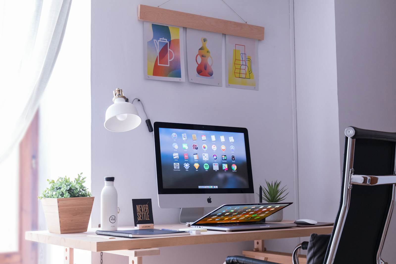 Monitor on a brown wooden desk beside a small plant in bright daylight