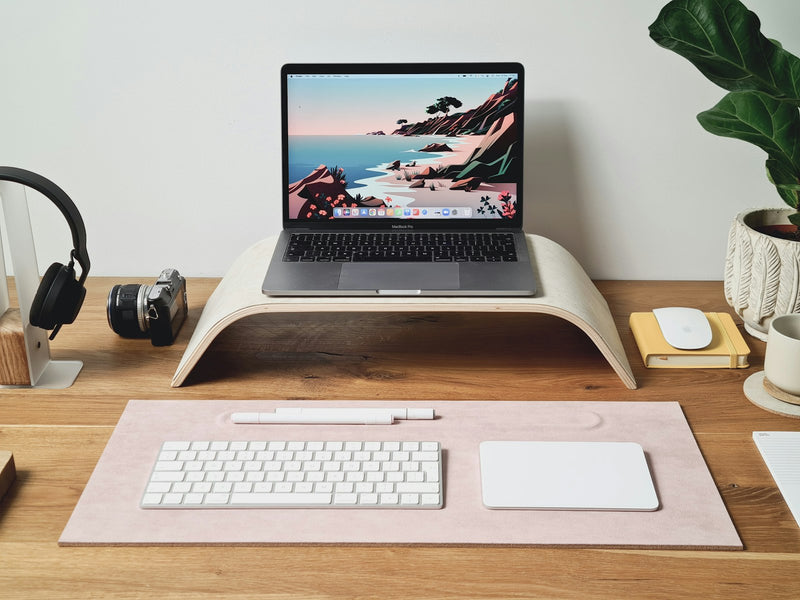 Minimal wooden desk with a laptop on a raised stand and a few considered objects